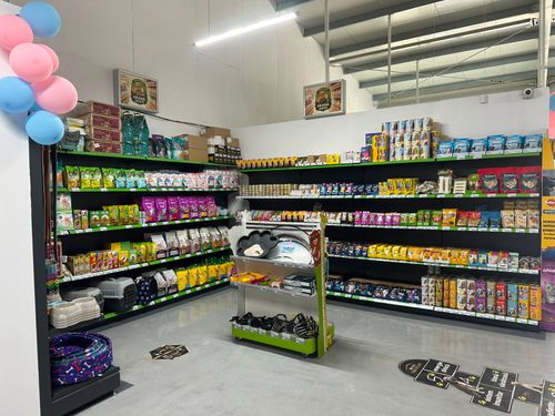 Raft cu hrană uscată și umedă pentru câini și pisici, plus cuști de transport și boluri, în petshop-ul Șendri Agrovet.
